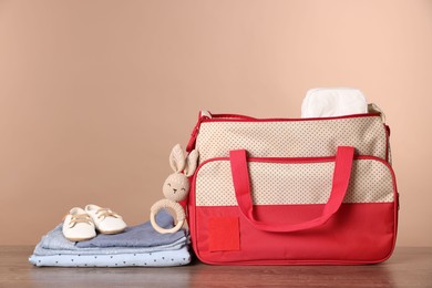 Photo of Mother's bag with baby's stuff on wooden table against beige background. Space for text