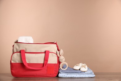 Mother's bag with baby's stuff on wooden table against beige background. Space for text