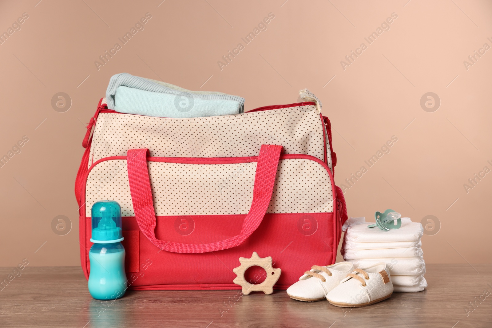 Photo of Mother's bag with baby's stuff on wooden table against beige background