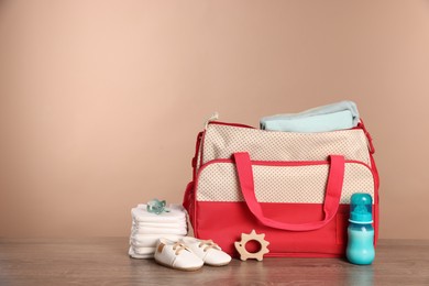 Mother's bag with baby's stuff on wooden table against beige background. Space for text