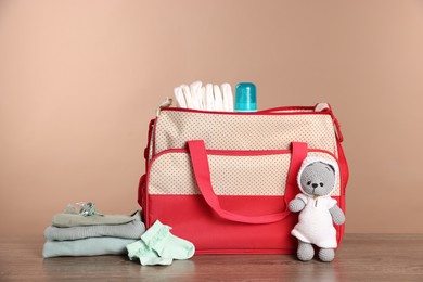 Photo of Mother's bag with baby's stuff on wooden table against beige background