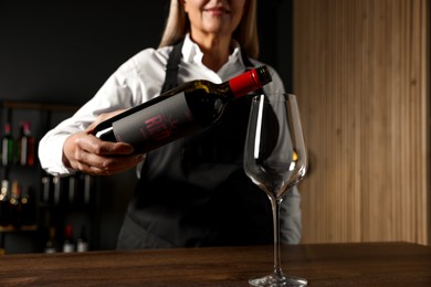 Photo of Professional sommelier pouring red wine into glass at wooden table indoors, closeup