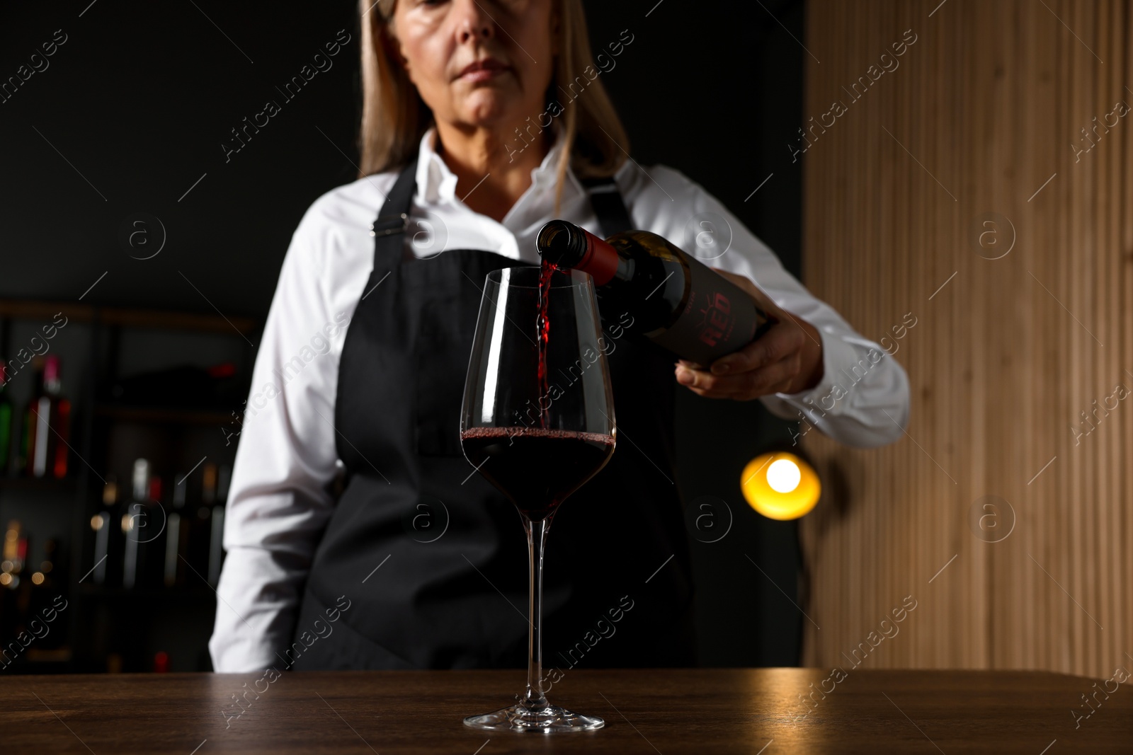 Photo of Professional sommelier pouring red wine into glass at wooden table indoors, selective focus