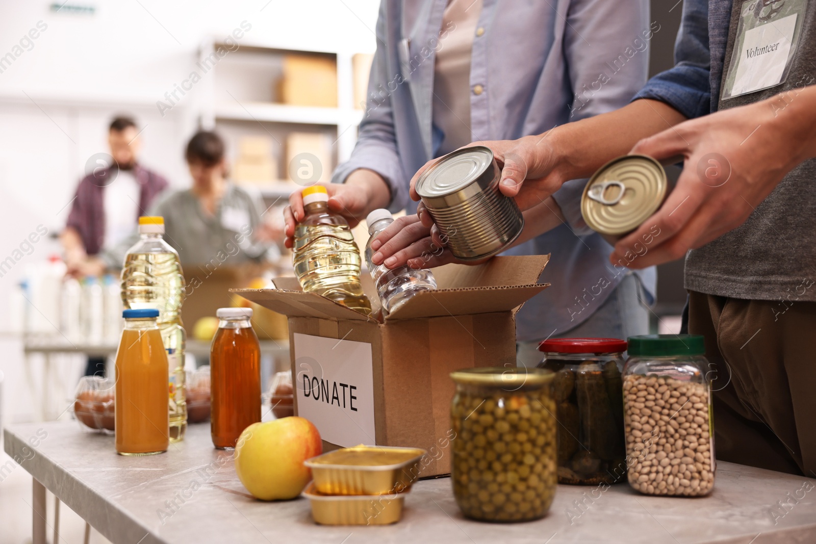 Photo of Volunteers packing food donations at table indoors, closeup