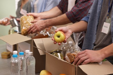 Photo of Group of volunteers packing food donations at table indoors, closeup