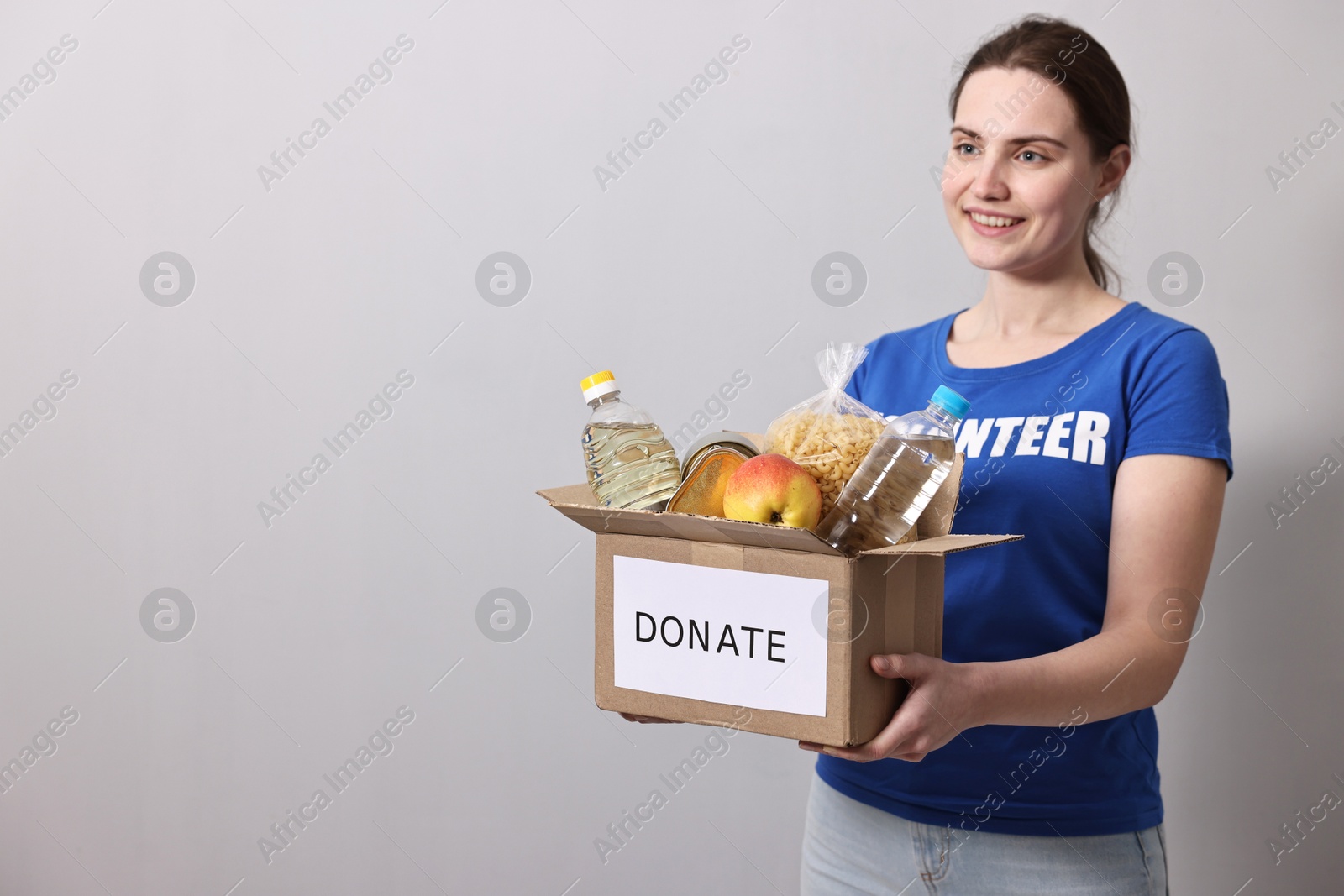 Photo of Woman holding donation box with food products on grey background, space for text