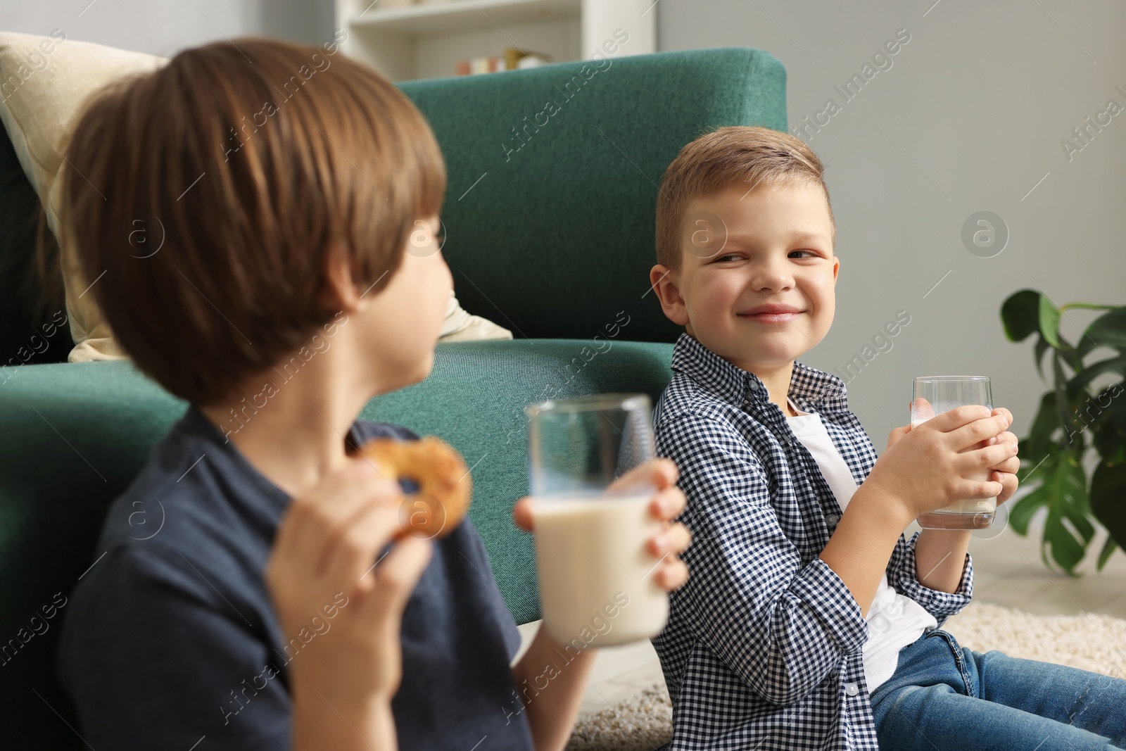 Photo of Cute brothers with glasses of milk and cookies at home, selective focus