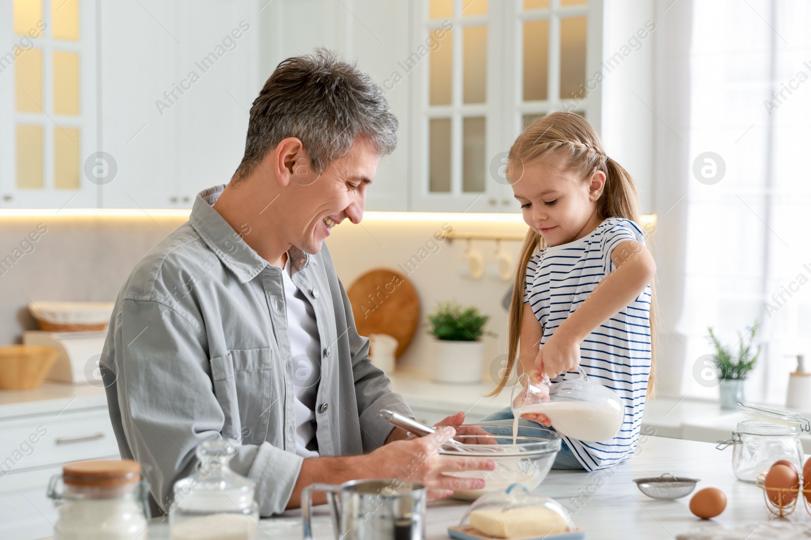 Photo of Father and his daughter making dough at white marble table in kitchen