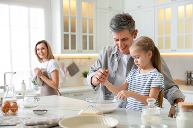 Photo of Happy parents and their daughter making dough at white marble table in kitchen