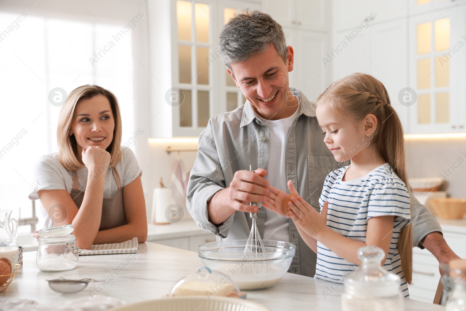 Photo of Happy parents and their daughter making dough at white marble table in kitchen