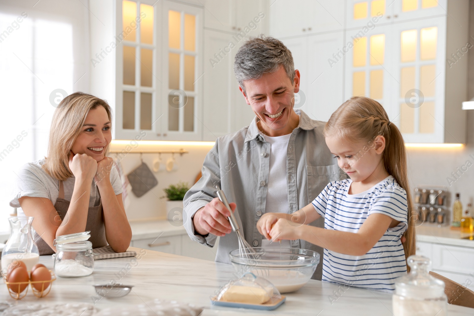 Photo of Happy parents and their daughter making dough at white marble table in kitchen