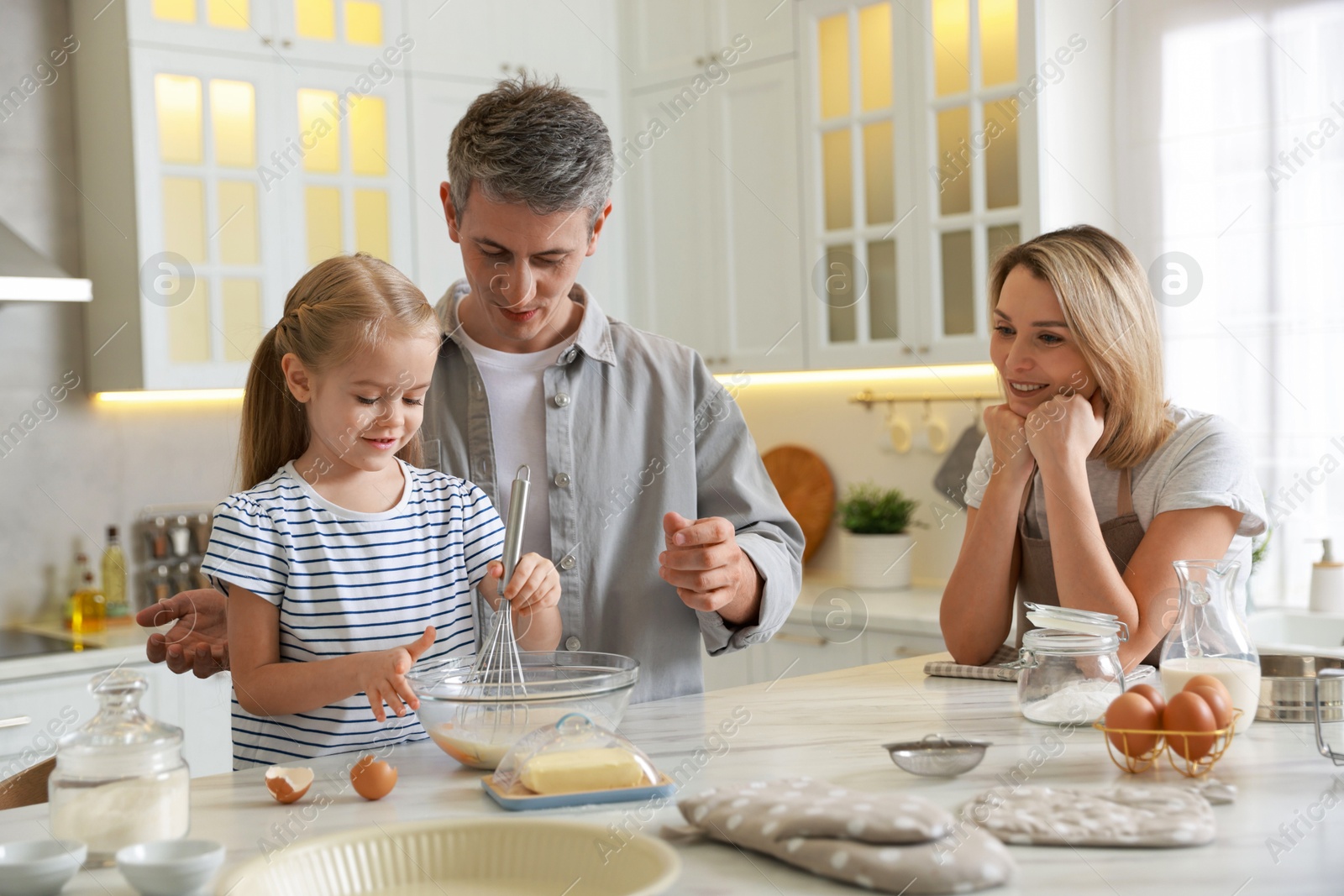 Photo of Happy parents and their daughter making dough at white marble table in kitchen