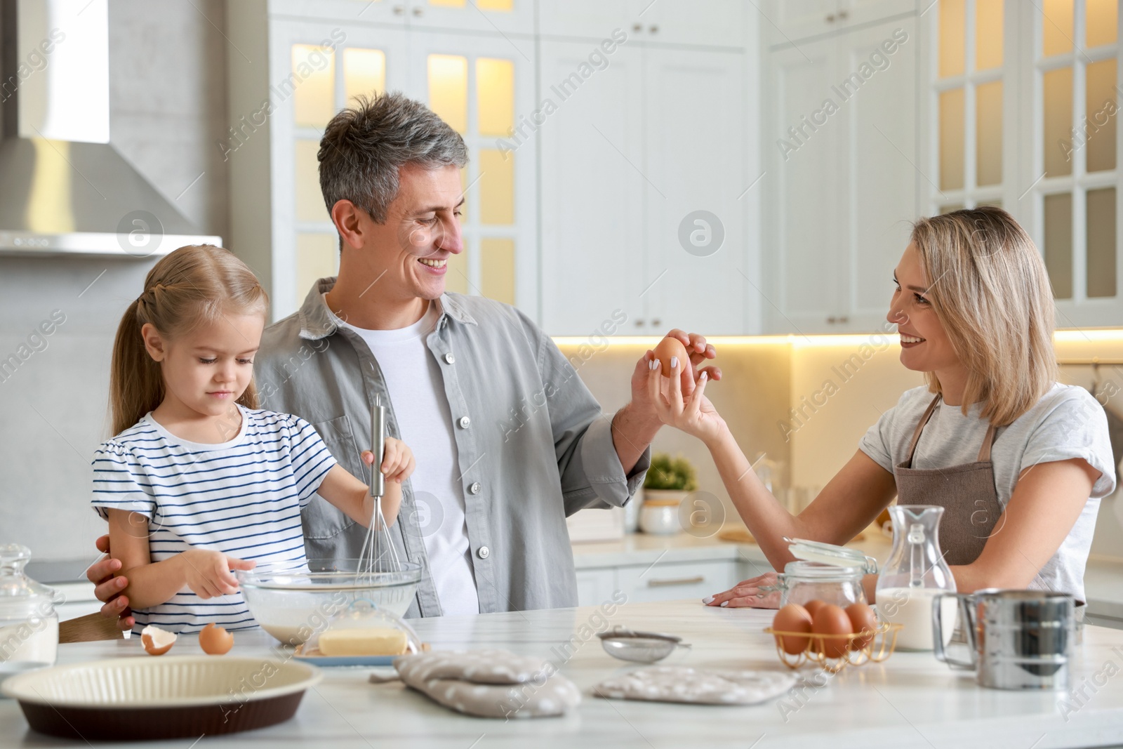 Photo of Happy parents and their daughter making dough at white marble table in kitchen