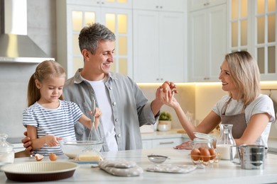 Photo of Happy parents and their daughter making dough at white marble table in kitchen