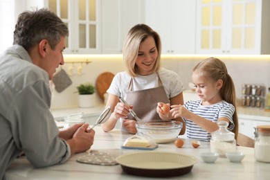 Photo of Happy parents and their daughter making dough at white marble table in kitchen