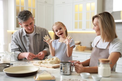 Photo of Happy parents and their daughter making dough at white marble table in kitchen