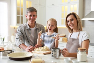 Photo of Happy parents and their daughter making dough at white marble table in kitchen