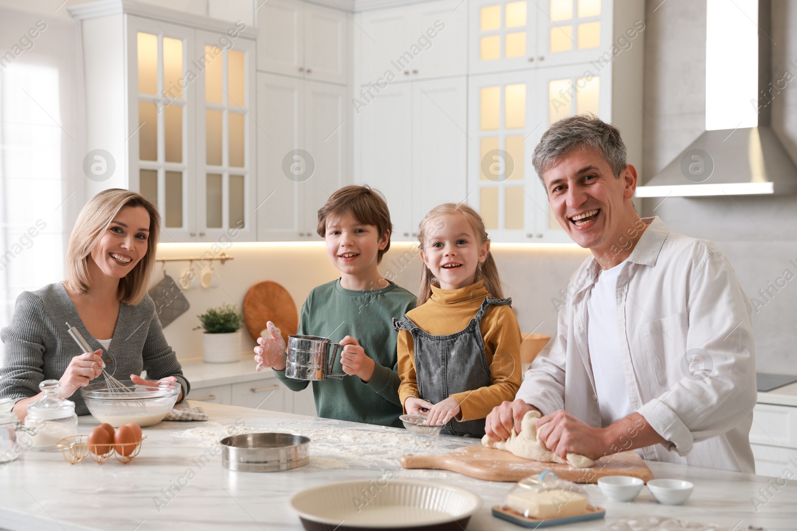 Photo of Happy family making dough at white marble table in kitchen