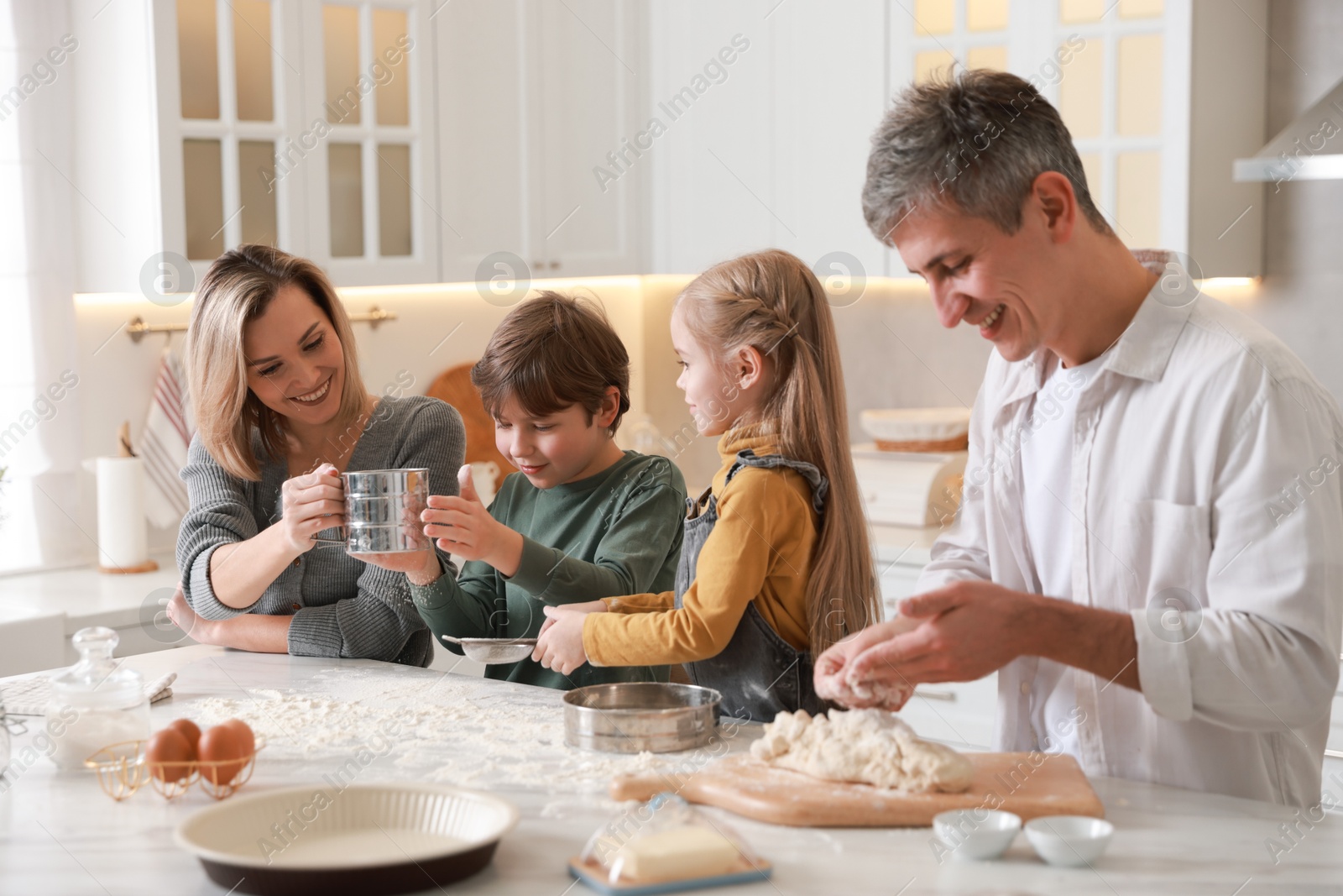 Photo of Happy family making dough at white marble table in kitchen