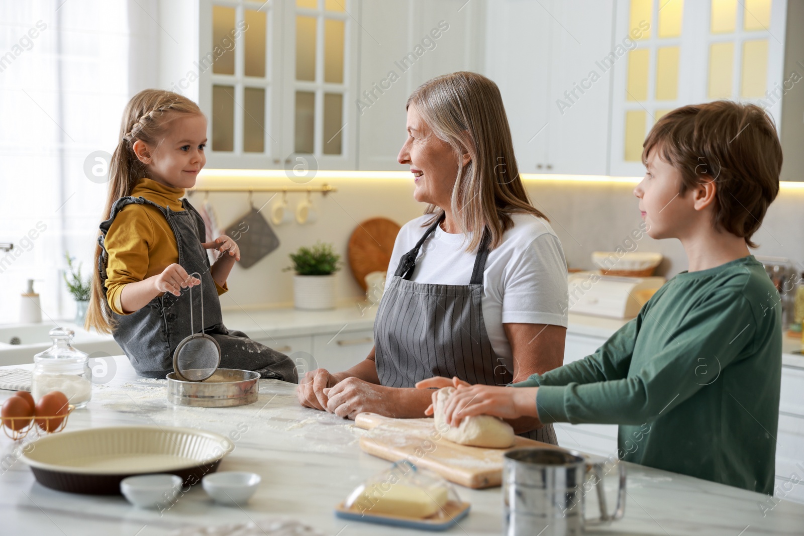 Photo of Grandmother and her grandchildren making dough at white marble table in kitchen