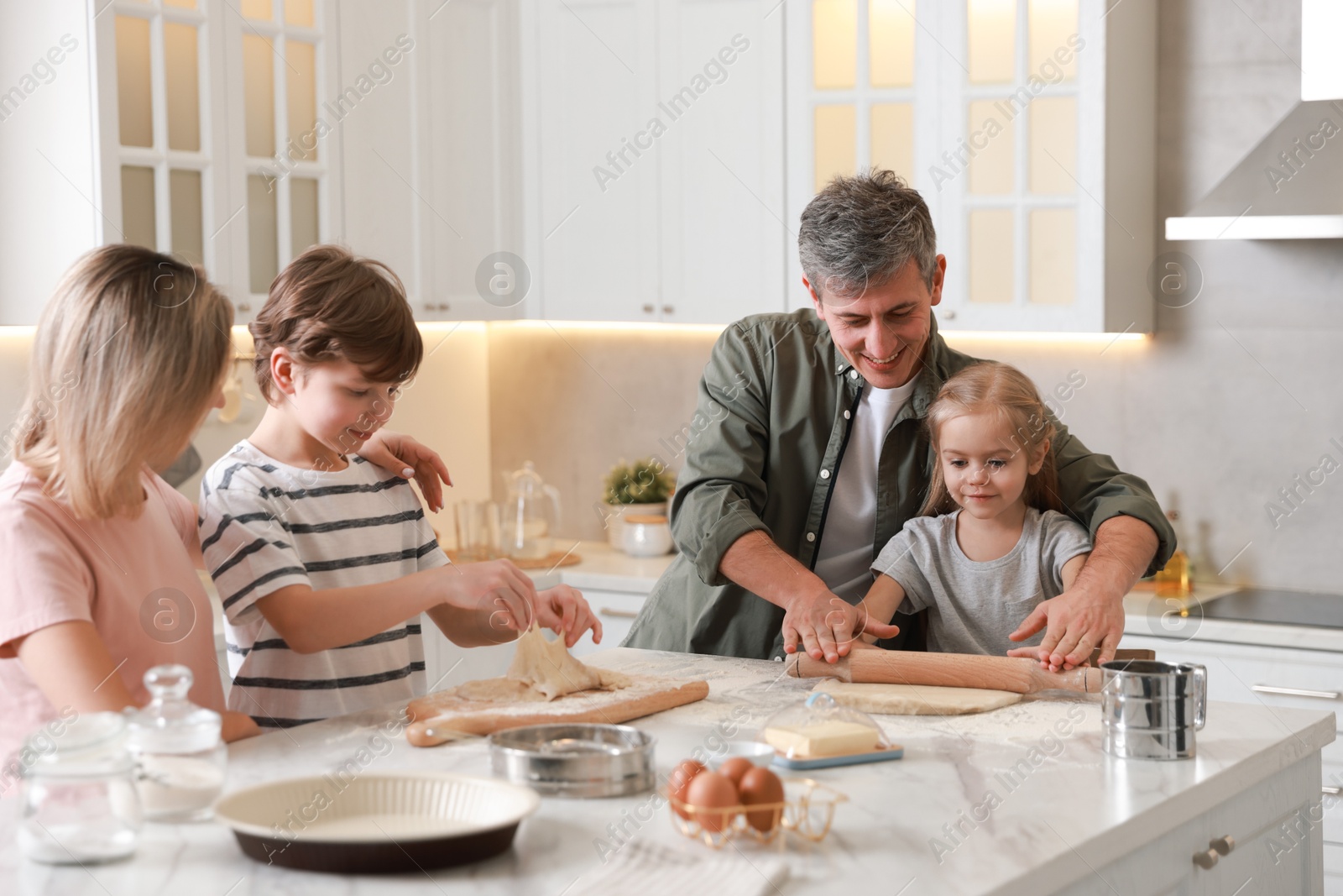 Photo of Happy family making dough at white marble table in kitchen