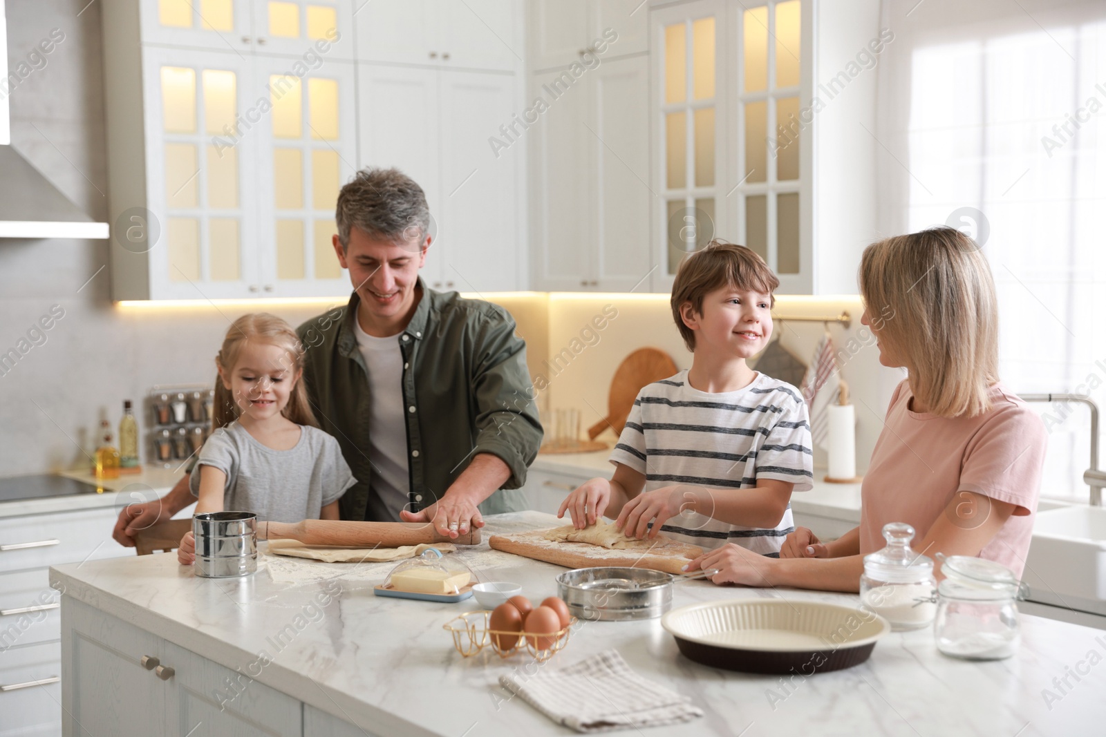 Photo of Happy family making dough at white marble table in kitchen