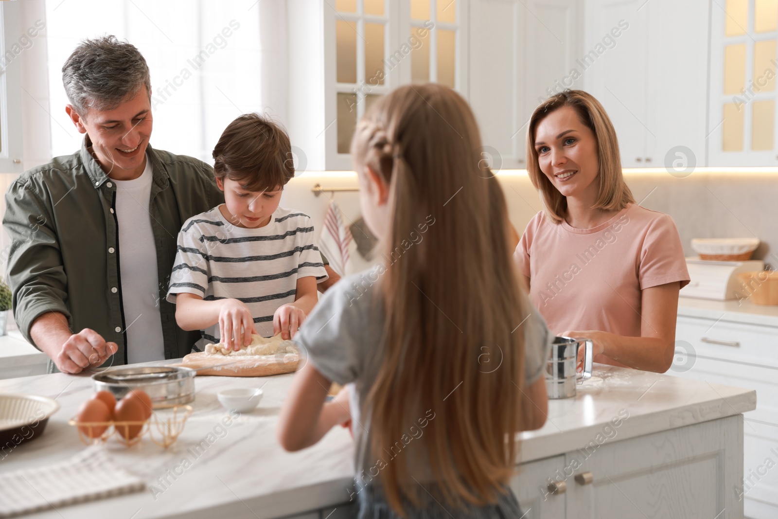 Photo of Happy family making dough at white marble table in kitchen