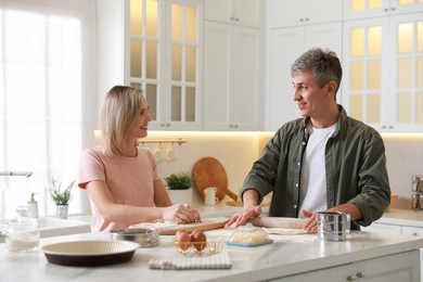 Happy couple kneading dough at white marble table in kitchen