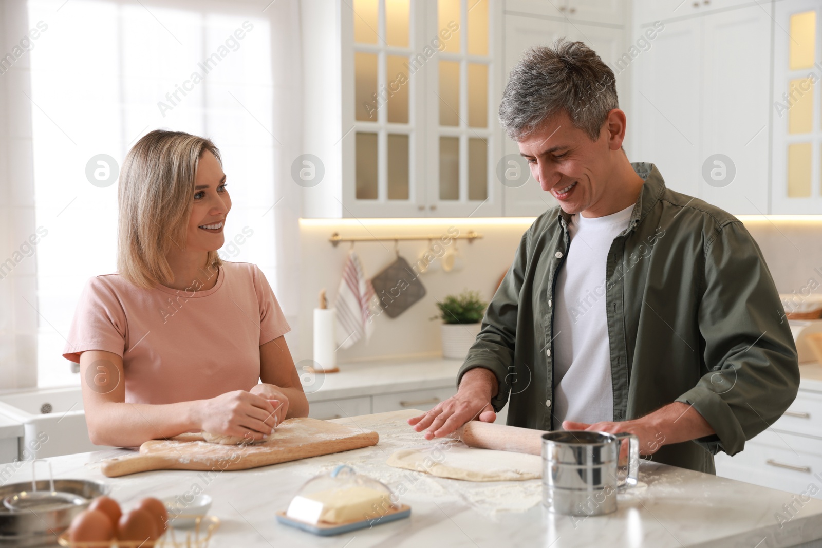 Photo of Happy couple kneading dough at white marble table in kitchen