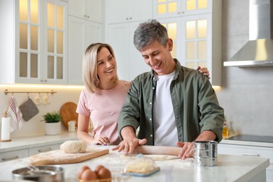 Photo of Happy couple shaping dough with rolling pin at white marble table in kitchen