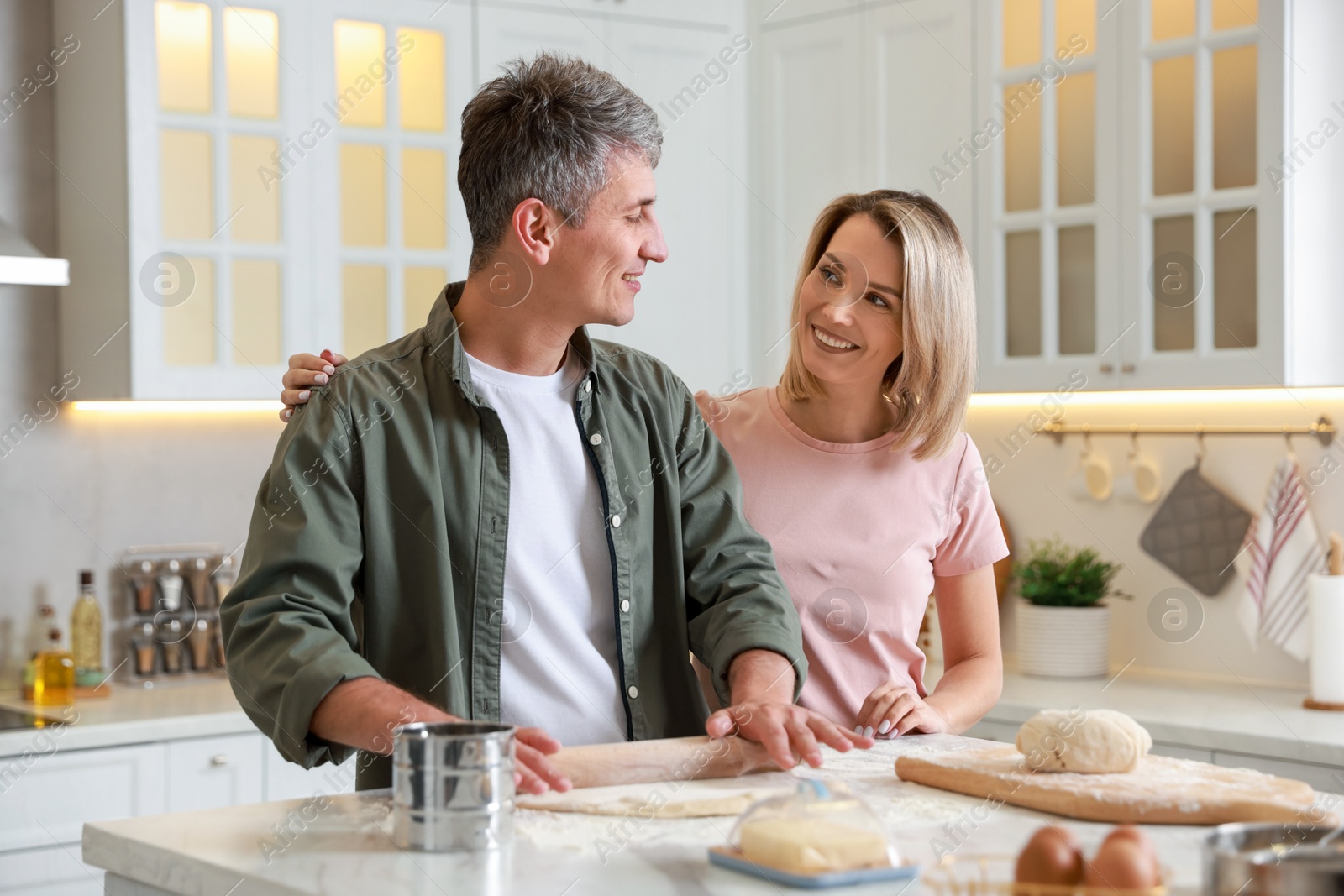 Photo of Happy couple shaping dough with rolling pin at white marble table in kitchen