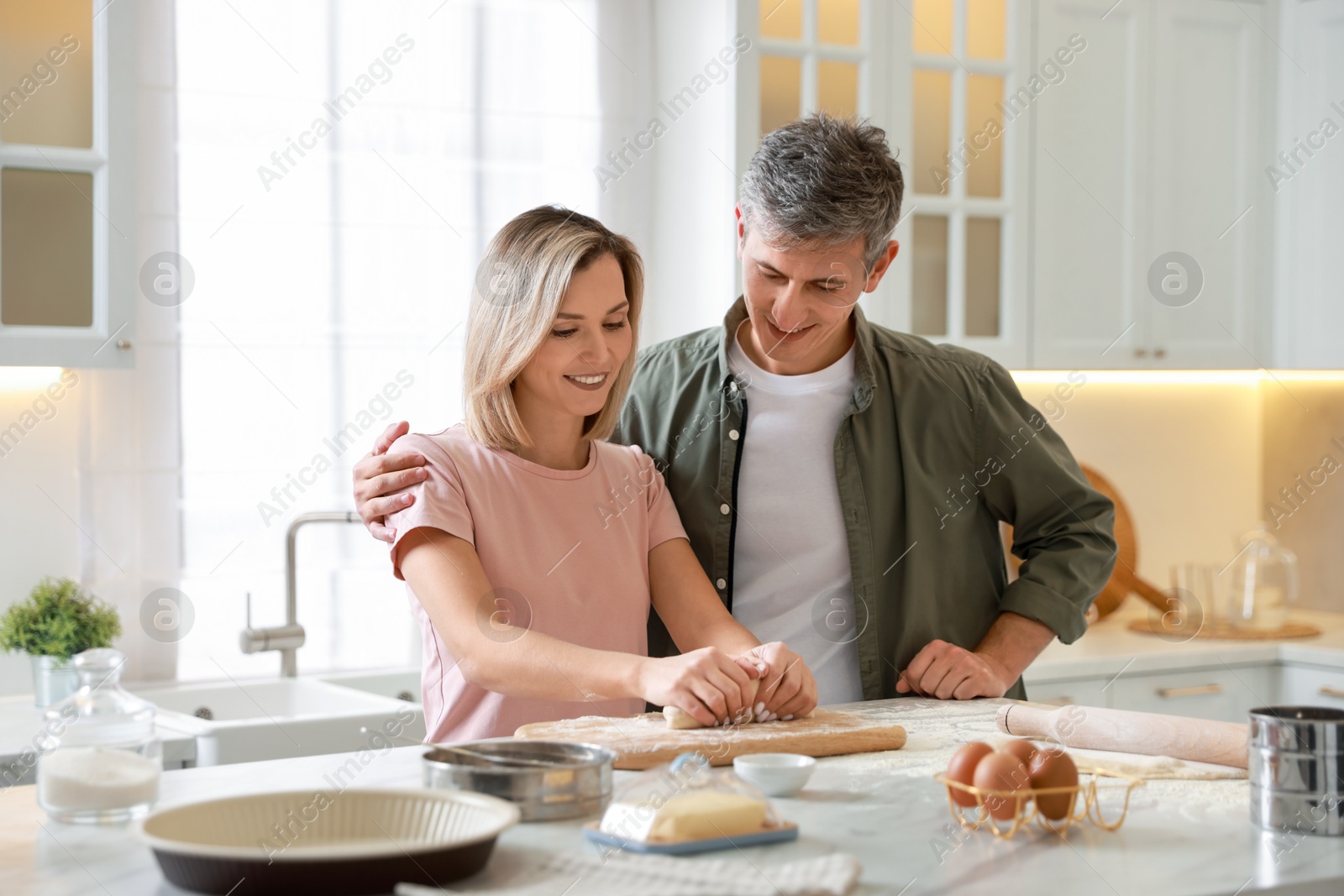 Photo of Happy couple kneading dough at white marble table in kitchen