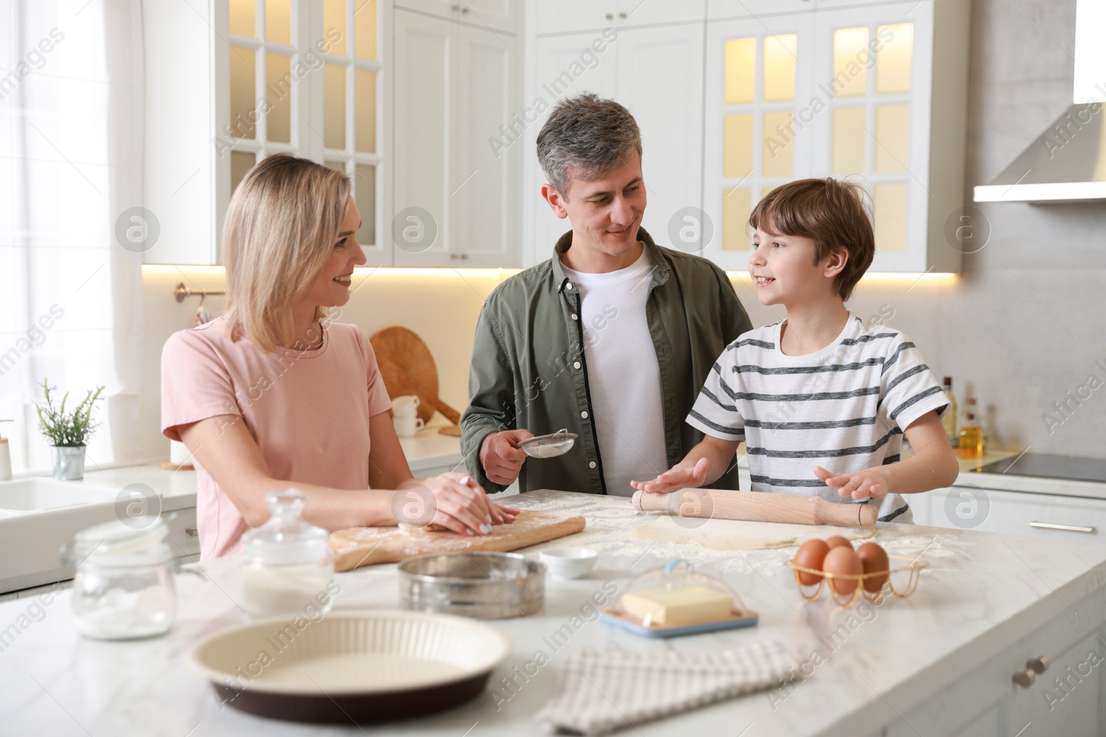 Photo of Happy family kneading dough at white marble table in kitchen