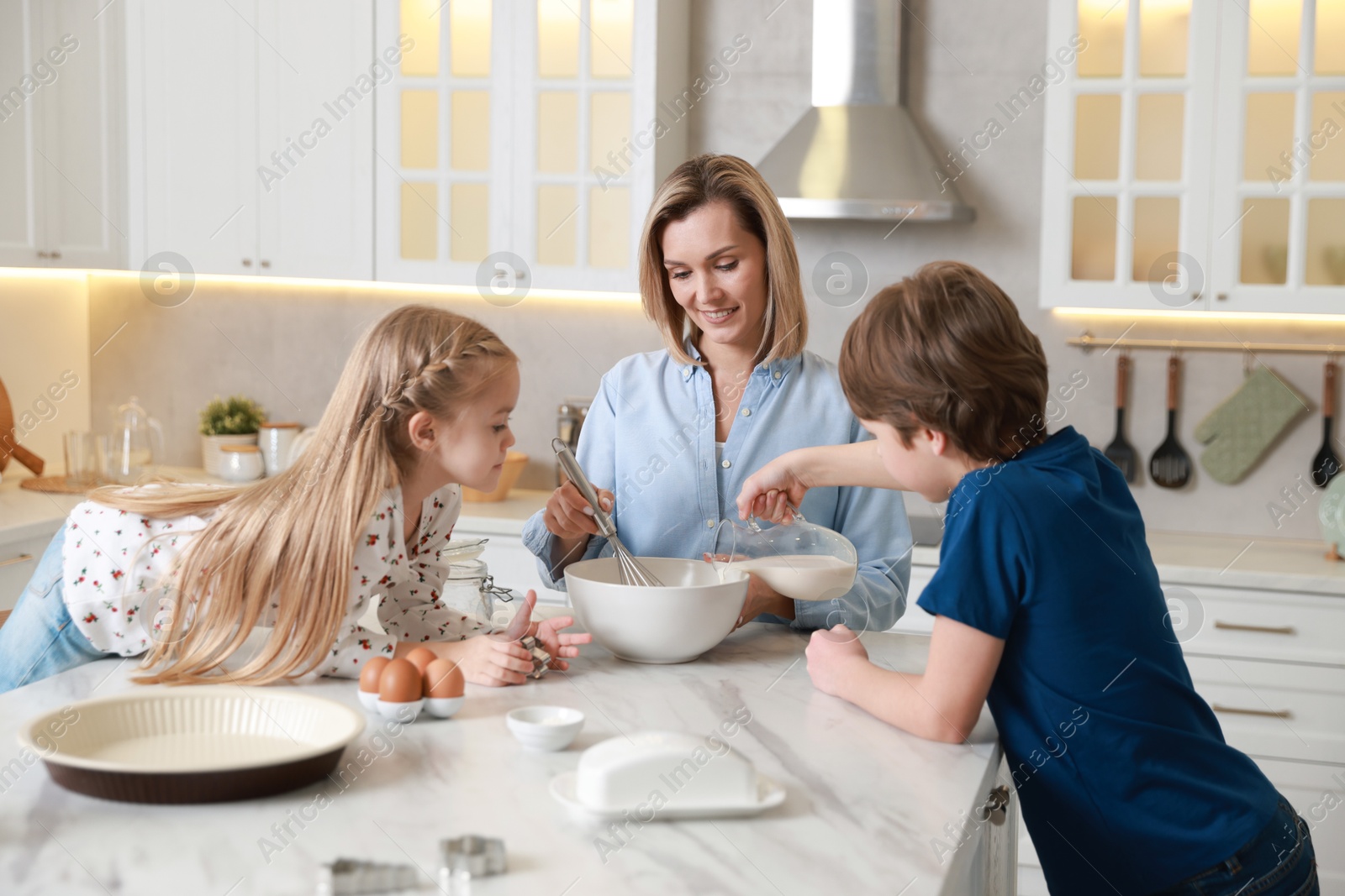 Photo of Mother and her kids making dough at white marble table in kitchen