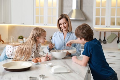 Photo of Mother and her kids making dough at white marble table in kitchen