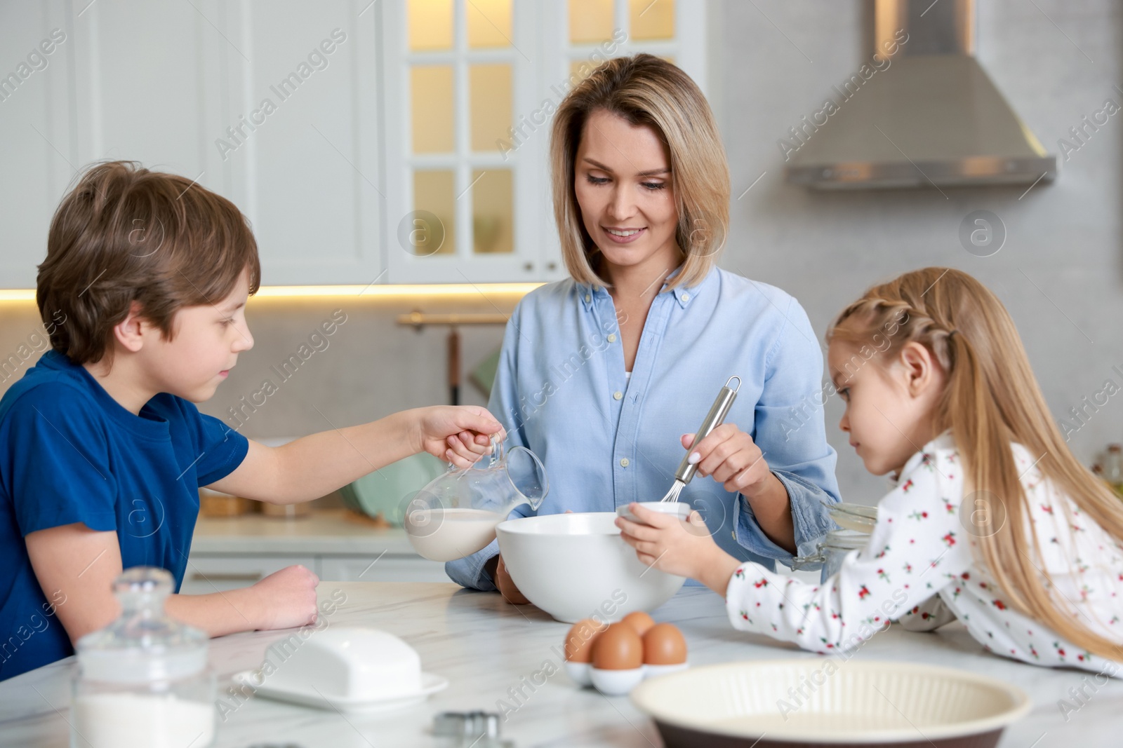 Photo of Mother and her kids making dough at white marble table in kitchen