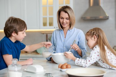 Photo of Mother and her kids making dough at white marble table in kitchen