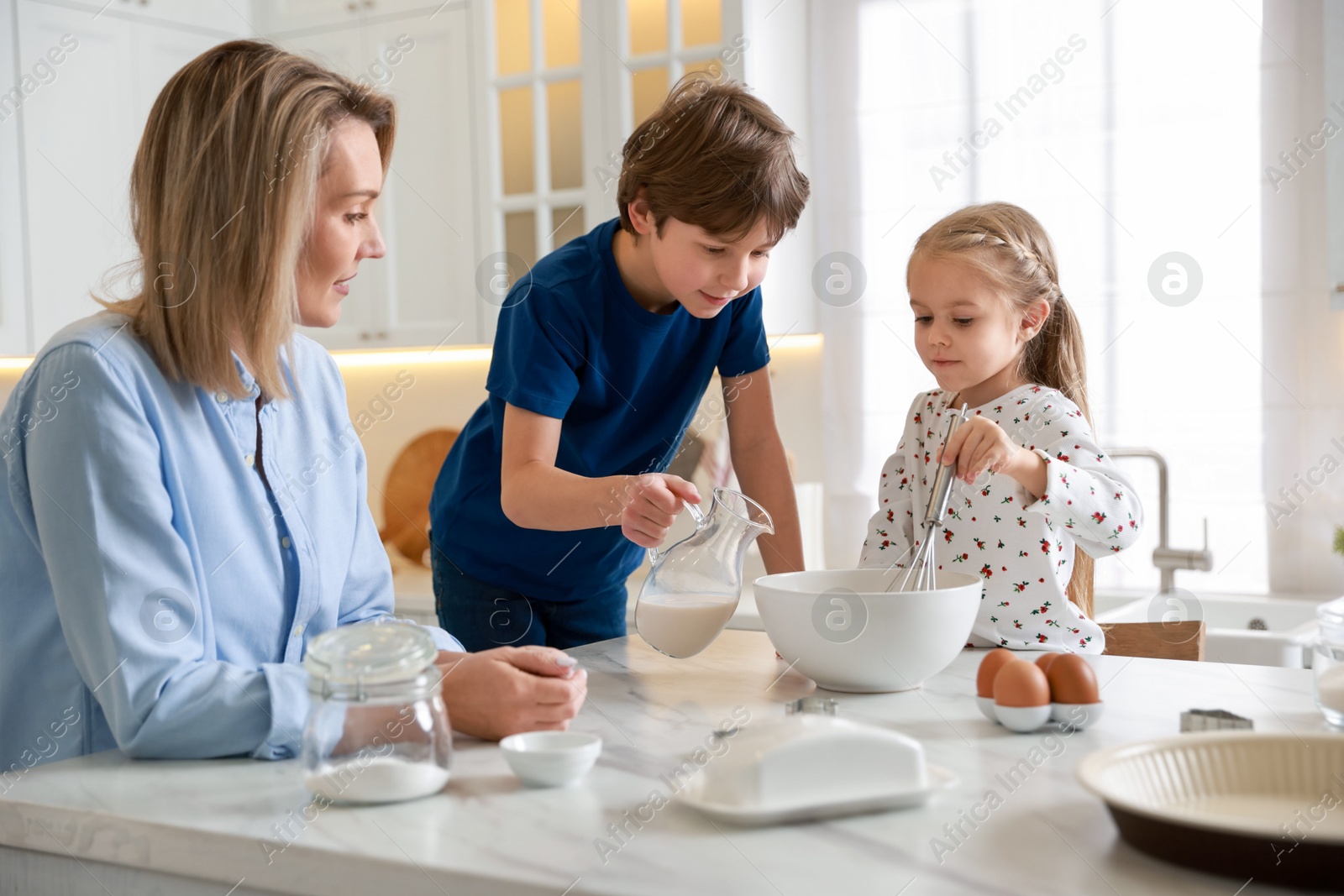 Photo of Mother and her kids making dough at white marble table in kitchen