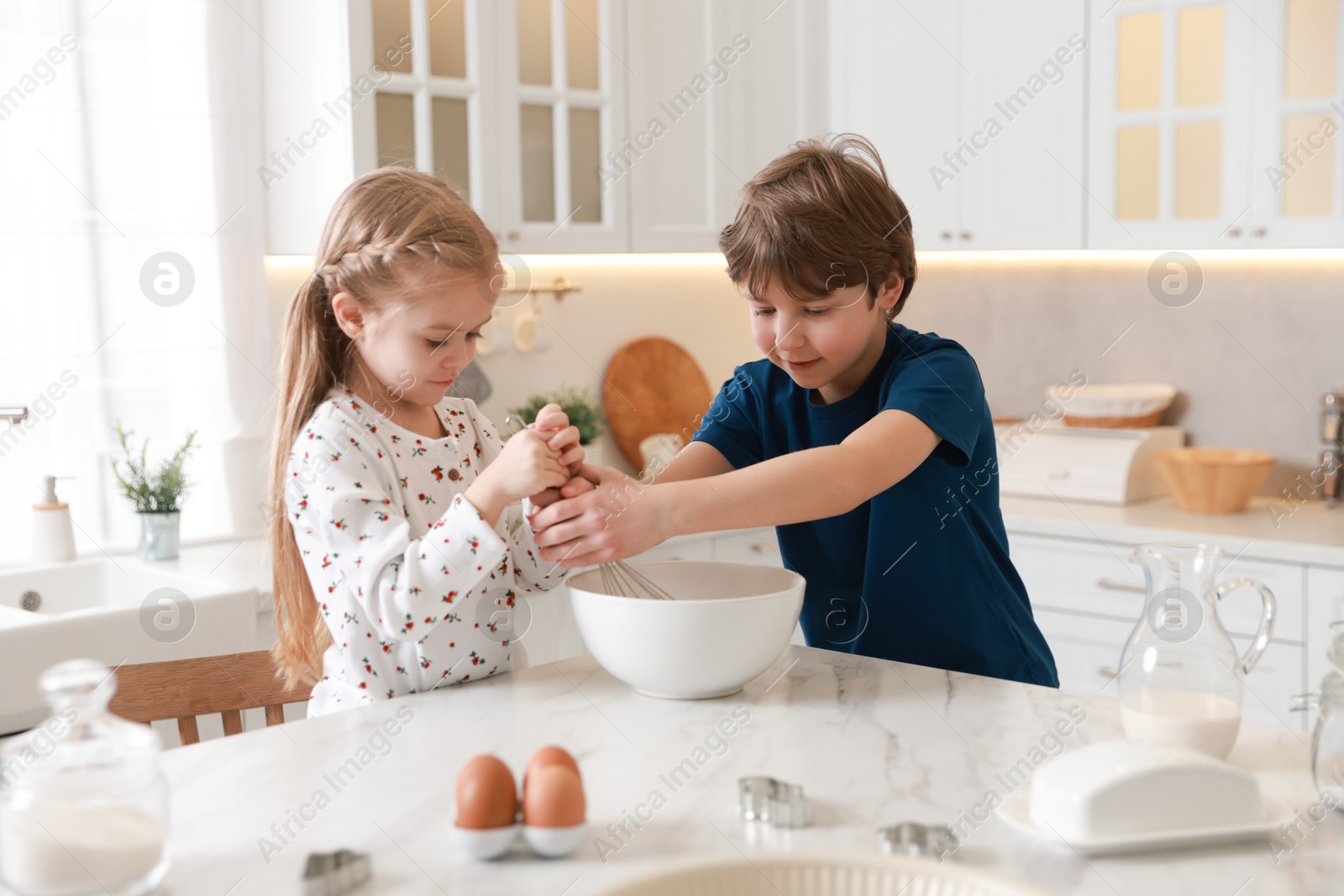 Photo of Little kids making dough at white marble table in kitchen