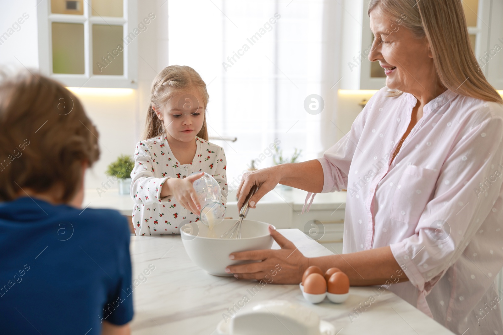 Photo of Grandmother and her grandchildren making dough at white marble table in kitchen