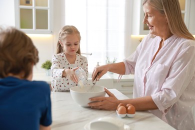 Photo of Grandmother and her grandchildren making dough at white marble table in kitchen