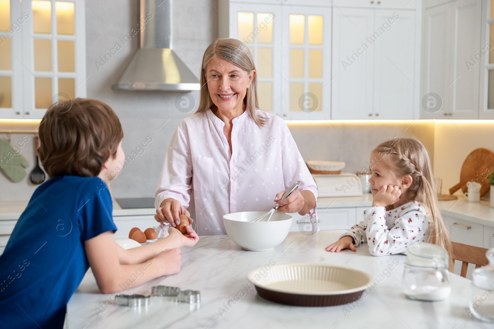 Photo of Grandmother and her grandchildren making dough at white marble table in kitchen