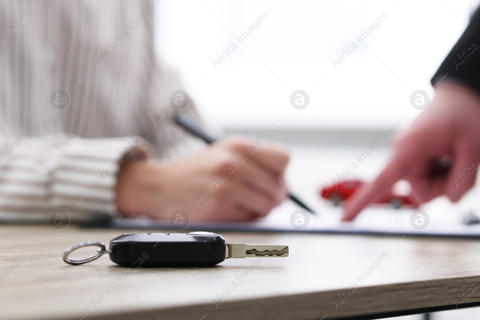 Photo of Salesman showing client where to sign car purchase agreement at wooden table indoors, focus on key. Buying auto