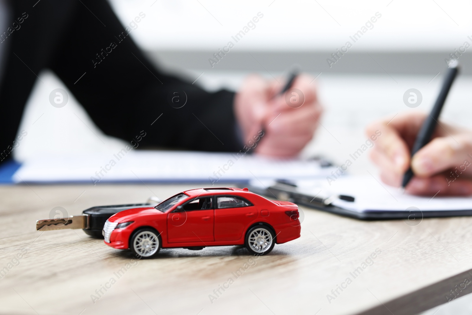 Photo of Salesman and client signing documents at wooden table, focus on car model and key. Buying auto