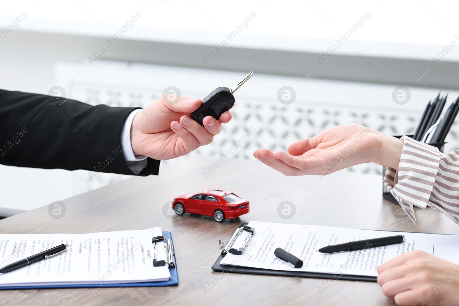 Photo of Salesman giving key to client at wooden table in office, closeup. Buying auto