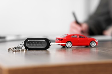 Photo of Buying auto. Car model and key on wooden table, selective focus