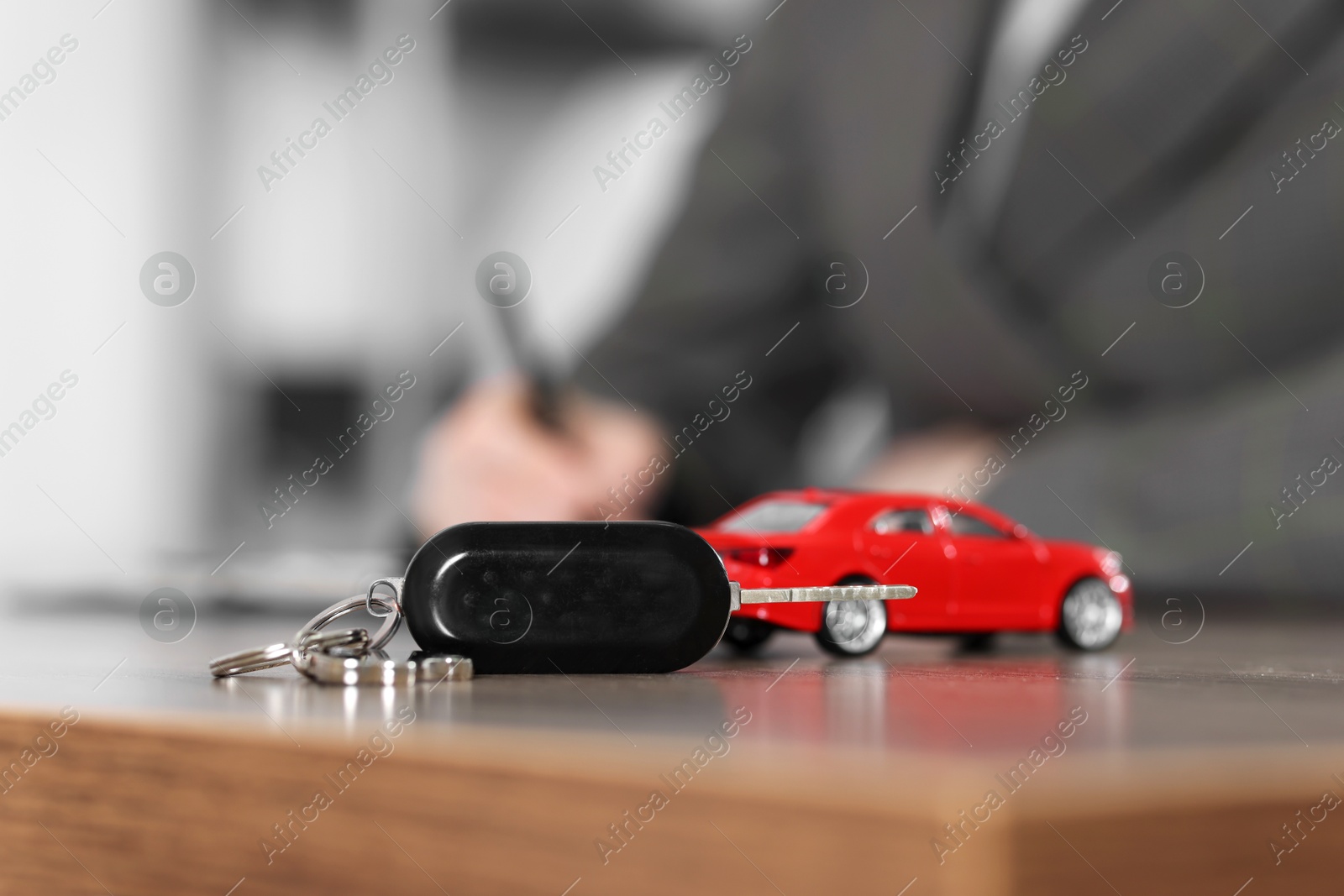 Photo of Buying auto. Car model and key on wooden table, selective focus