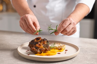 Photo of Professional chef serving dish at table indoors, closeup