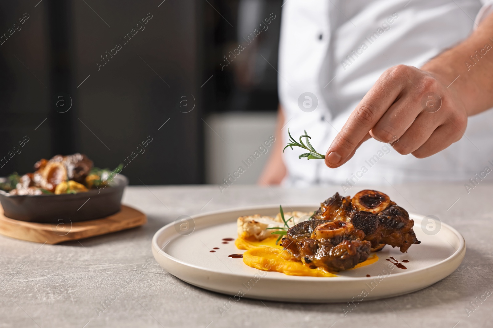 Photo of Professional chef serving dish at table indoors, closeup