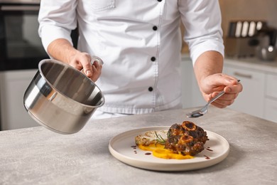 Photo of Professional chef adding sauce to delicious dish at table indoors, closeup